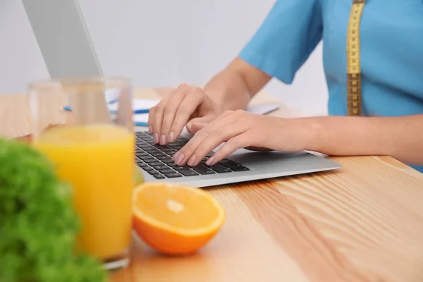 Молодая женщина-диетолог работает с ноутбуком в офисе, крупным планом — стоковое фото