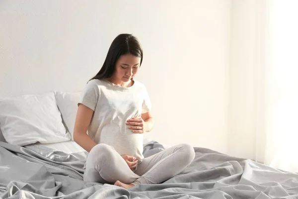 Femme asiatique enceinte assis sur le lit à la maison — Photo