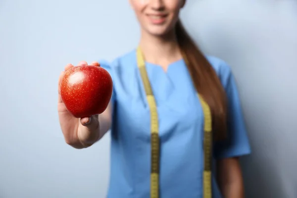 Unga kvinnliga nutritionist med apple på ljus färg bakgrunden, närbild — Stockfoto