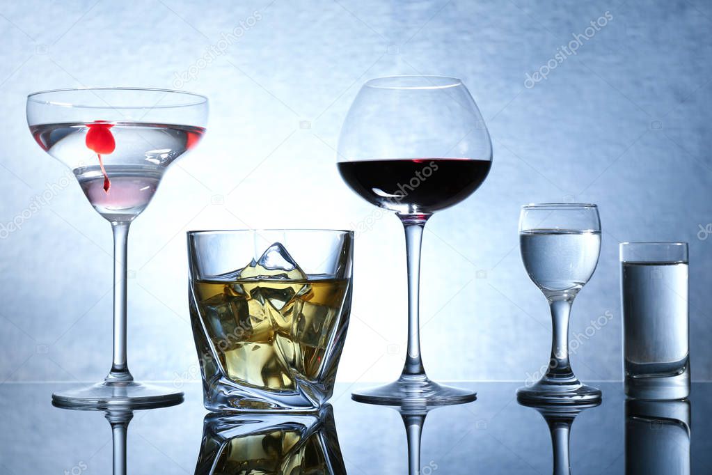 Different glasses of wine and spirits on color background