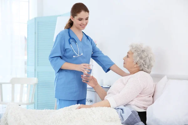 Nurse giving glass of water to elderly woman — Stock Photo, Image