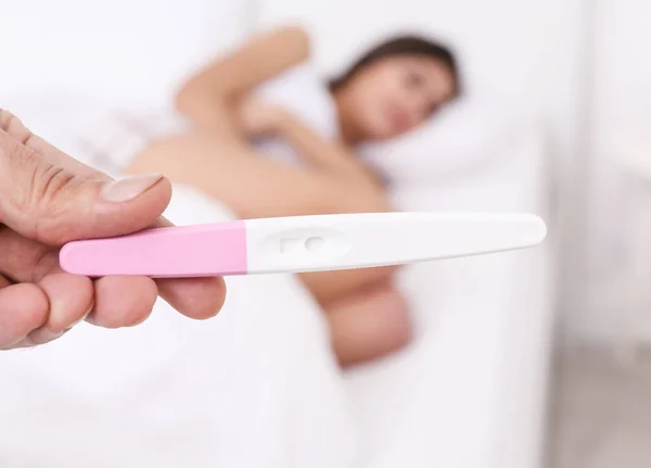 Male hand with pregnancy test and blurred woman on background — Stock Photo, Image