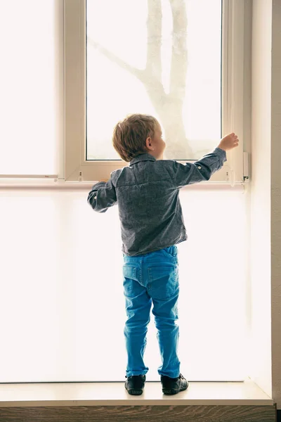 Söt liten pojke står på fönsterbrädan hemma — Stockfoto