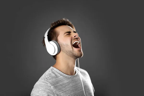 Emotional man with headphones listening music on grey background — Stock Photo, Image