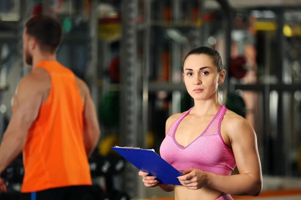 Entrenador personal sujetando portapapeles con plan de entrenamiento en gimnasio — Foto de Stock