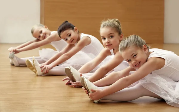 Skupina krásné malé baletky dělá cvičení na podlaze — Stock fotografie