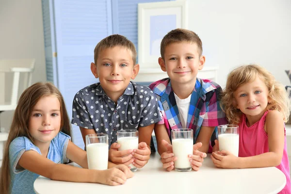 Crianças com copos de leite sentadas à mesa na sala — Fotografia de Stock