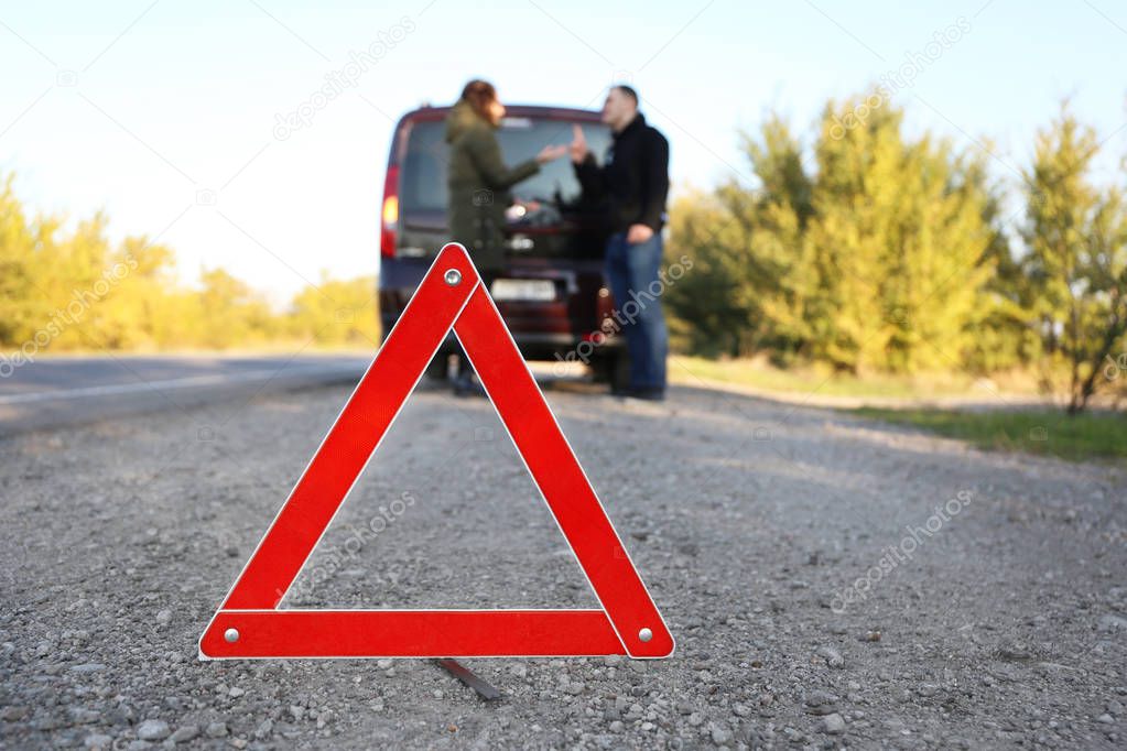 Red warning triangle on asphalt road. Couple near broken down car