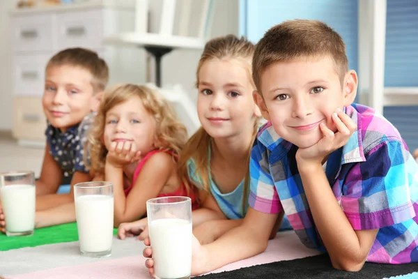 Fröhliche Kinder mit Milchgläsern, die auf buntem Teppich im Raum liegen — Stockfoto