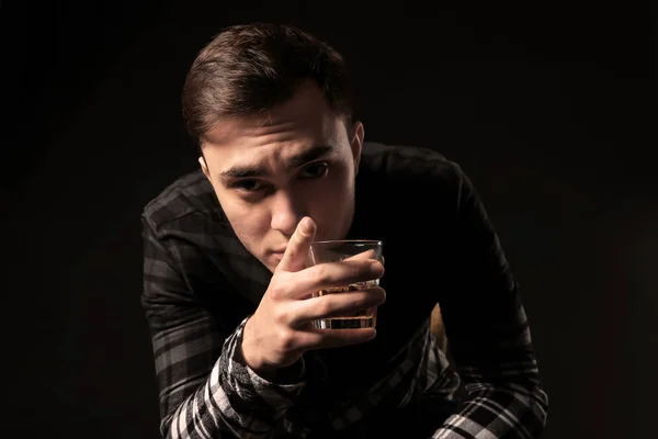 Bel homme déprimé avec un verre d'alcool sur fond noir — Photo