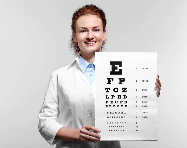 Young doctor holding eyesight test chart on grey background — Stock Photo, Image