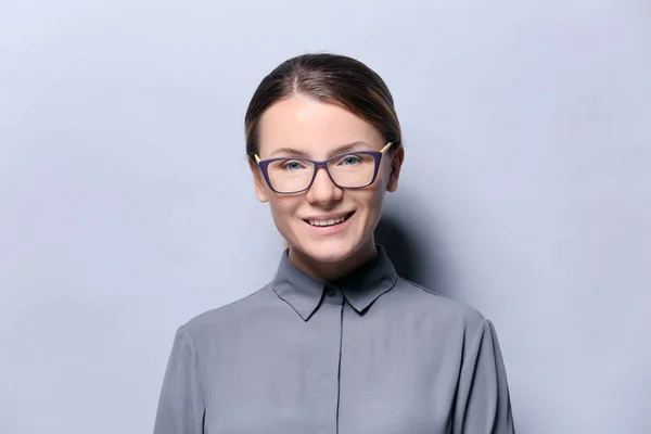 Mladá žena s brýlemi na šedém pozadí — Stock fotografie