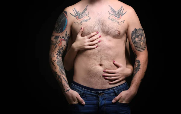 Hombre tatuado con una mujer manos en el cuerpo, fondo negro — Foto de Stock