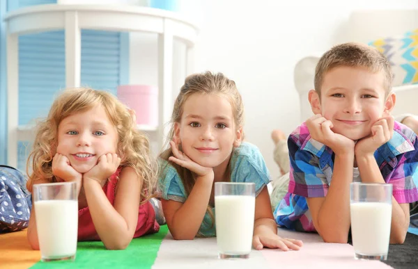 Crianças alegres com copos de leite deitado no tapete colorido na sala — Fotografia de Stock