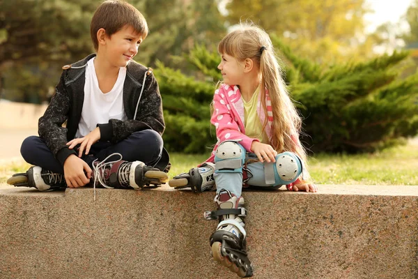 Cheerful friends in roller skates sitting on border in park — Stock Photo, Image