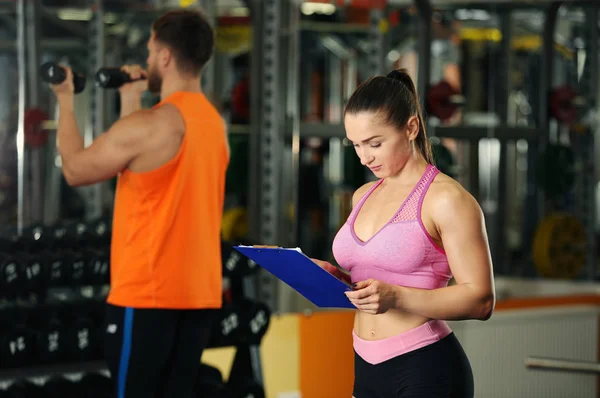 Personlig tränare håller Urklipp med träningsprogram i gymmet — Stockfoto