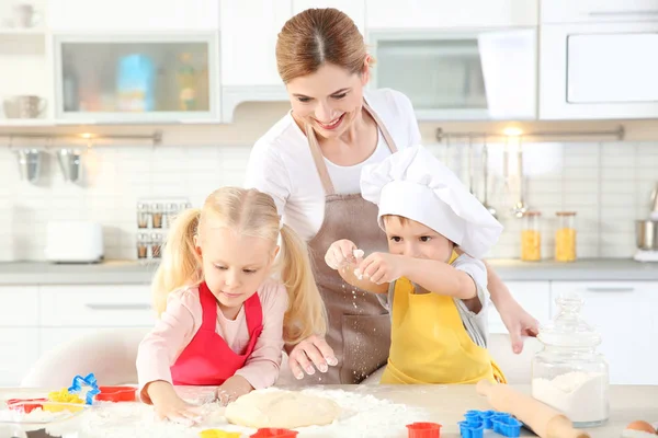 Madre joven con niños haciendo galletas en la mesa —  Fotos de Stock