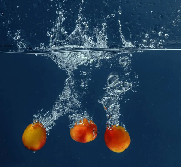 Свежие абрикосы, падающие в воду — стоковое фото