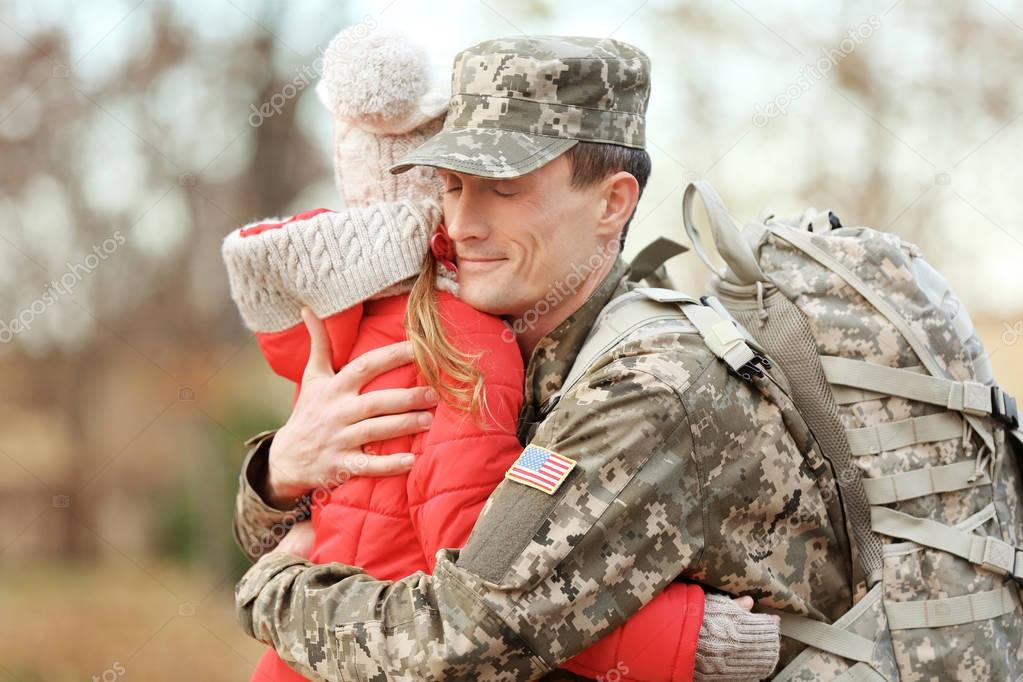 Soldier in camouflage hugging daughter outdoors