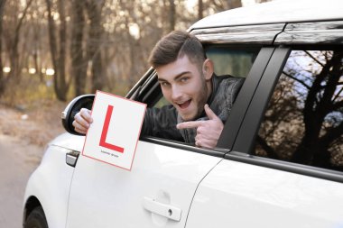 Genç adam araba pencereden dışarı bakarken öğrenen şoför işaret tutan