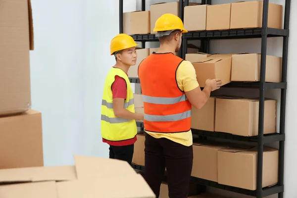 Werknemers in de buurt van plank met cartoon dozen in magazijn — Stockfoto