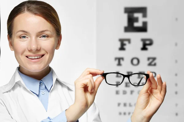 Mujer joven sosteniendo gafas en el fondo de la tabla de prueba de la vista — Foto de Stock