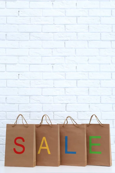 Palabra colorida VENTA en bolsas de compras de papel contra fondo de pared de ladrillo —  Fotos de Stock