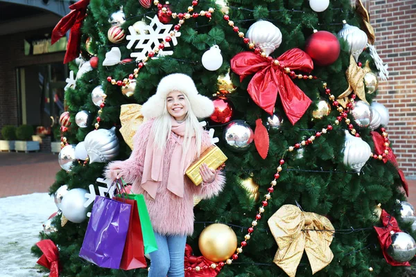 Женщина с подарочной коробкой и пакеты для покупок на фоне елки — стоковое фото