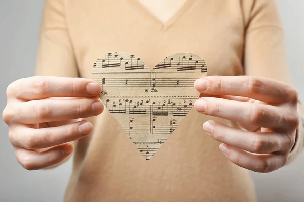 Mani femminili che tengono il cuore di carta con note, concetto musicale — Foto Stock