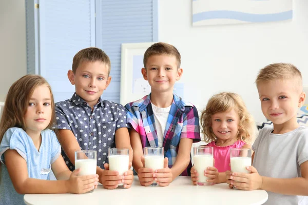 Children with glasses of milk sitting at table in the room — Stock Photo, Image