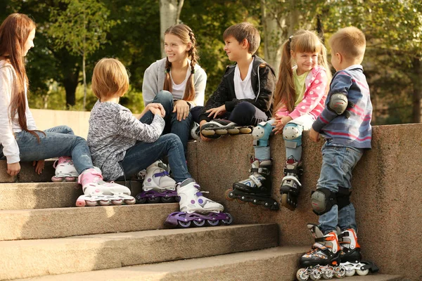 Cheerful friends in roller skates sitting on border in park — Stock Photo, Image