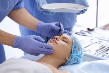 Plastic surgeon drawing marks on female face in clinic clipart