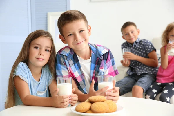 Kleine Jungen und Mädchen mit Milchgläsern sitzen am Tisch im Zimmer — Stockfoto