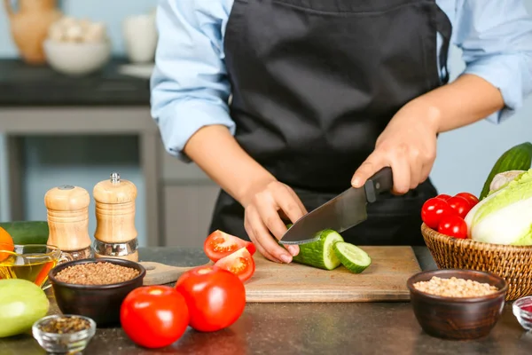 Vrouwelijke handen komkommer snijden aan tafel in de keuken — Stockfoto