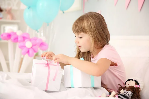 Cute birthday girl opening boxes with presents while sitting on bed at home — Stock Photo, Image