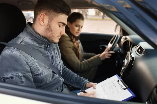 Instructor of driving school giving exam while sitting in car with young woman