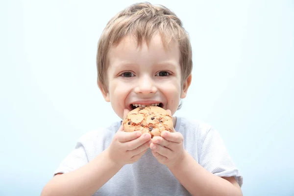 Cute little boy eating cookie on light background