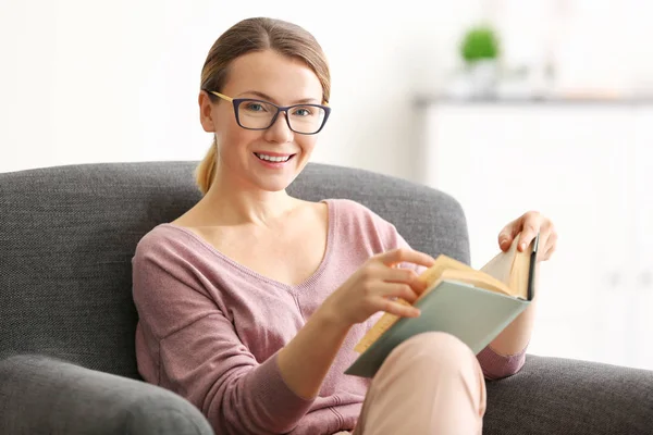 Jonge vrouw lezen boek op fauteuil — Stockfoto