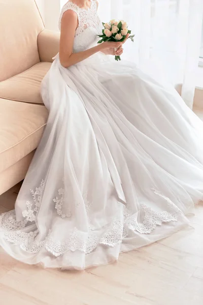Brud i vackra klänning med bröllop bukett sitter på soffa — Stockfoto