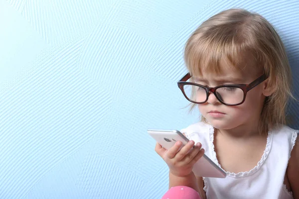 Милая маленькая девочка в очках и мобильный телефон на цветном фоне — стоковое фото