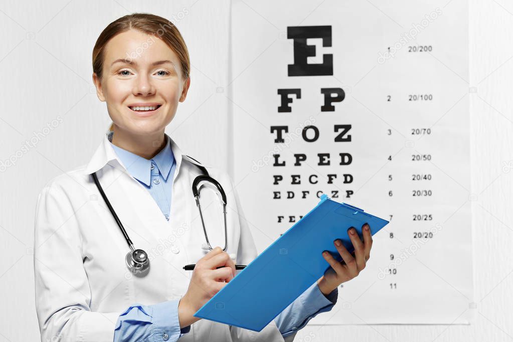 Young happy female doctor with clipboard on eyesight test chart background