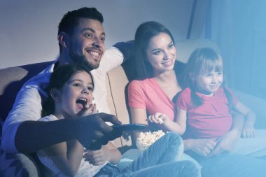 Mutlu bir aile evdeki kanepede televizyon izliyor.