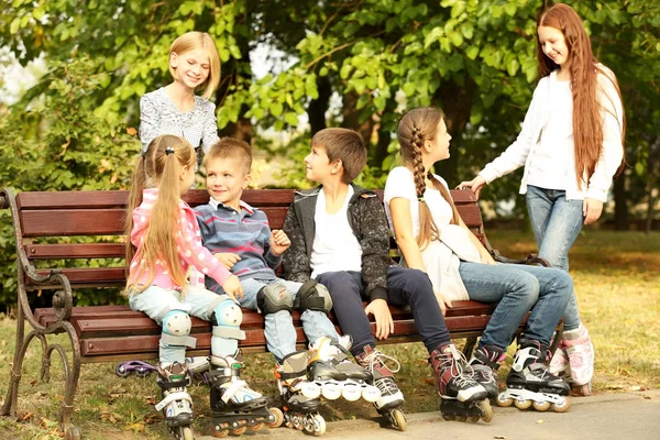 Crianças alegres com patins sentados no banco no parque — Fotografia de Stock