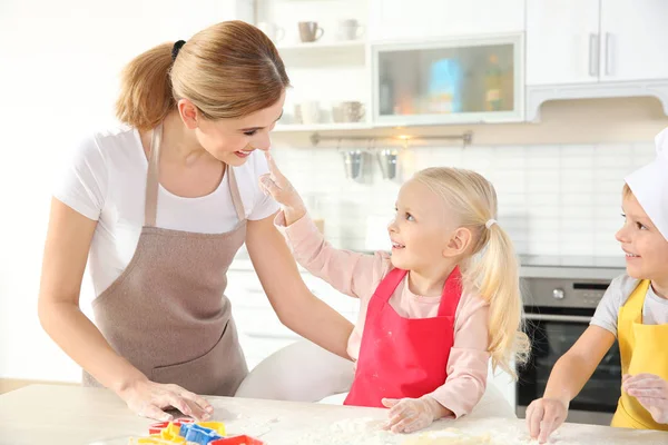 Молодая мама с детьми делает печенье на столе — стоковое фото