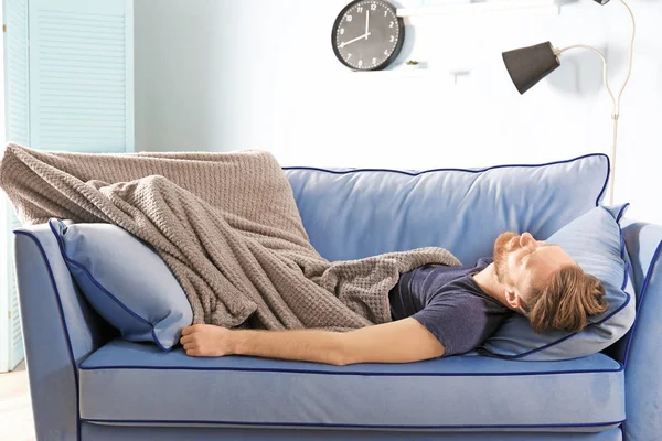 Jovem com cobertor dormindo no sofá em casa — Fotografia de Stock