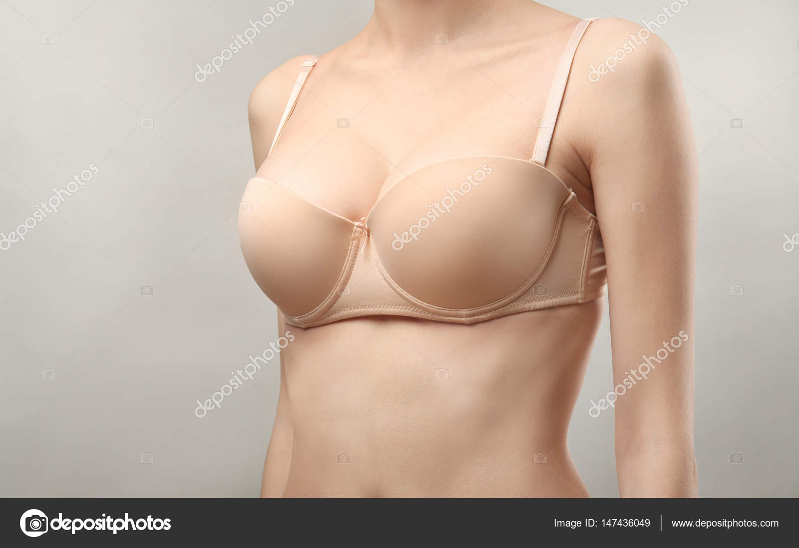 Young tanned woman in black bra before and after breast augmentation with  silicone implants. The result of a breast lift. Breast size correction  isolated on a gray background. Plastic surgery concept Stock