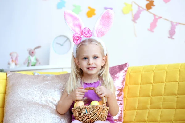 Sepet dolu evde koltukta oturan Paskalya yumurta ile sevimli küçük kız — Stok fotoğraf