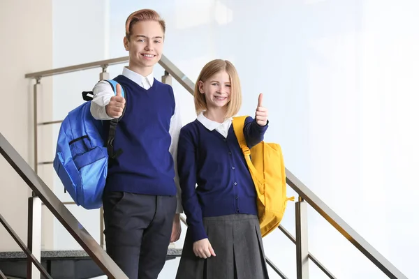 Mignon garçon et fille en uniforme scolaire debout sur les escaliers et montrant pouce vers le haut geste — Photo