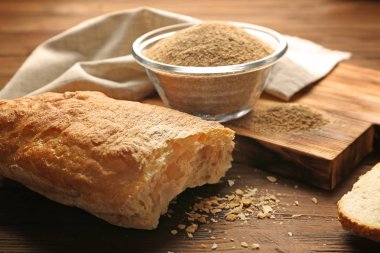 Glass bowl of bread crumbs and broken loaf on wooden table clipart