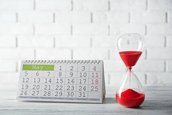 Hourglass with red sand and calendar — Stock Photo, Image